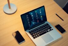 Mesa de trabalho organizada com smartphone, laptop e caderno abertos, exibindo aplicativos de produtividade em destaque.