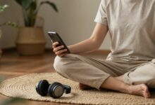 Pessoa relaxando em posição de meditação com um smartphone na mão e fones de ouvido, rodeada por elementos naturais e uma sensação de tranquilidade