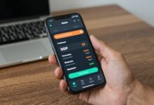 Usuário segurando smartphone com aplicativos de comparação de preços abertos, mostrando gráficos e etiquetas de desconto