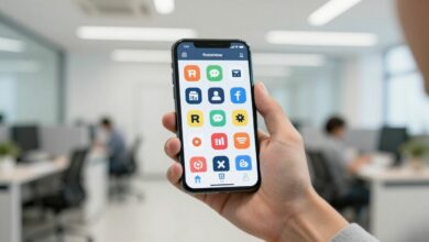A person's hand holding a smartphone displaying various sales and e-commerce app icons, with a blurred background of a modern office.