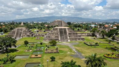 Uma visão panorâmica da grandiosa cidade asteca de Tenochtitlán, com suas pirâmides imponentes, canais e jardins flutuantes (chinampas) sob um céu dramático.