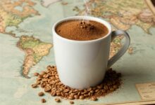 Uma xícara de café fumegante sobre grãos de café torrados, com um mapa antigo ao fundo, simbolizando a jornada histórica da bebida pelo mundo.