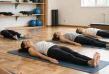 Uma pessoa praticando Pilates em casa sobre um tapete de yoga, em uma sala iluminada e organizada, focada na execução correta de um exercício de solo.