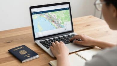 Viajante planejando uma viagem econômica com laptop aberto em uma busca de voos, mapa de destinos, caderno de anotações e passaporte sobre uma mesa iluminada.